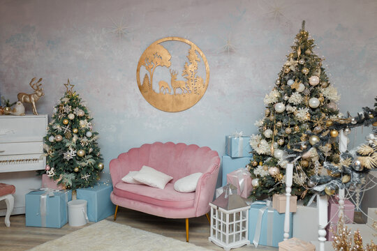 Christmas and New Year celebration. Pink sofa, two fir-trees and wooden picture with reindeers on wall. Holiday spirit, waiting for miracle. Modern decorated room interior.
