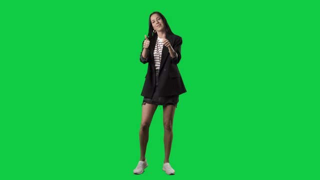 Happy playful stylish woman in suit jacket showing thumbs up gestures. Full body isolated on green screen background