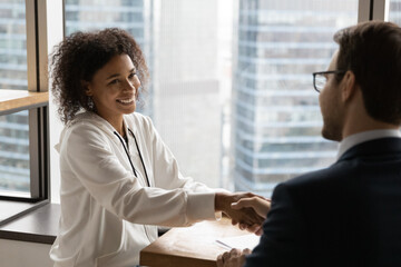Smiling young female african american job seeker shaking hands with confident male hr manager...