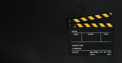 Black with yellow Clapper board or movie slate and black face mask on black blackground.