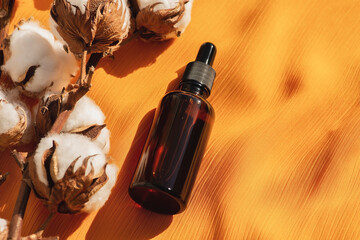 Amber glass dropper bottles with black lid with cotton flowers on yellow fabric background....