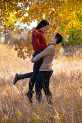 Lesbian couple with woman being held in the air looking down and smiling during autumn.