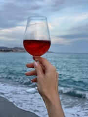 person with glass of wine in the sea on sunset