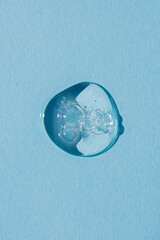 Transparent drop of cosmetic product serum gel. Liquid texture with bubbles on blue background in top view