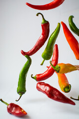 red, orange, green, yellow hot chili peppers, which are  flying on a white background 