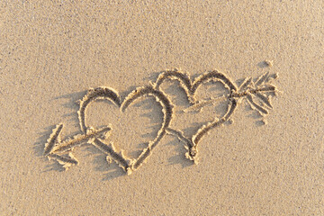 Drawing in the sand. Two hearts pierced by an arrow.