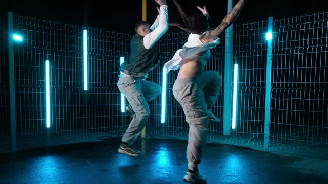 Group of two urban dancers performing outdoors with neon light stands. Street dance. Afrohouse. Talented man and woman enjoy life with dance. Slow motion in 4K, UHD