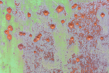 The surface of a rusty metal sheet with traces of green paint and bullet dents.   Textured background