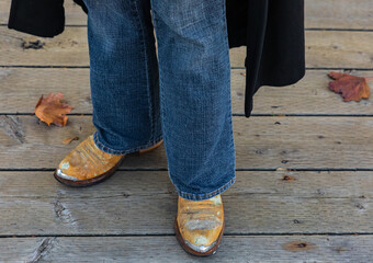 Cowboy boots and jeans, close up of details of Western style clothing on man outdoor. Autumn season.