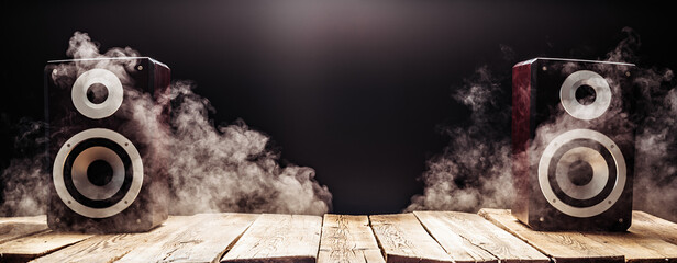 Two smoky audio speakers on wooden planks in the dark