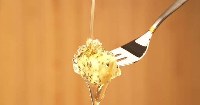 Liquid Organic Honey Dripping on a Fork with Dorbly Cheese on a Light Background. Healthy Food Concept. Golden Honey Pouring and Flowing on Cheese with Green Mold