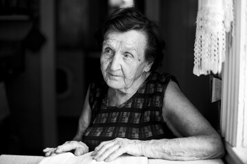 An old women sitting and reading the book in the kitchen at her home. Black and white photo.