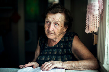 An old women sitting and reading the book in the kitchen at her home.