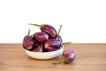 Mini eggplants in white plate on wooden table