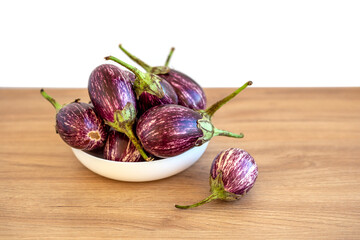 Mini eggplants in white plate on wooden table
