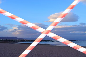 entry ban of the sea beach by fenced off with a red and white barrier tape. Concept of closed resorts and hotel beaches on quarantine. Coronavirus Concept of COVID pandemic and travel.