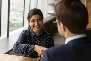 Smiling skilled beautiful young female indian applicant shaking hands with male boss leader,...