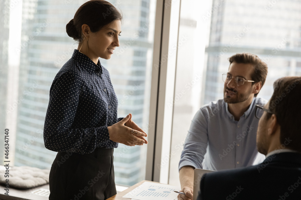 Canvas Prints Happy beautiful young indian businesswoman presenting project ideas to interested colleagues at boardroom. Smiling skilled female speaker leading negotiations meeting with employees in modern office.