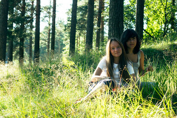 Naklejka na ściany i meble Two teen girl friends on the green grass in a summer park.