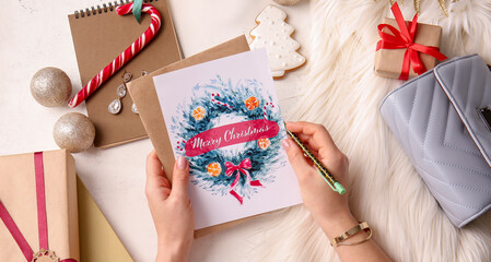Female hands with creative Christmas card and decor on light background