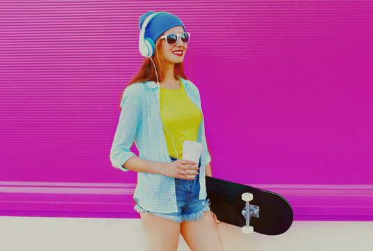 Summer image of smiling young woman with skateboard listening to music in headphones on colorful pink background