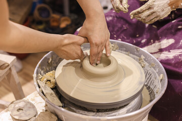 Learning Pottery Workshop. Closeup of teacher woman artist hands, learn student mold clay on pottery wheel. Creative handmade craft. Ceramic art studio.