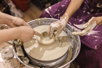 Learning Pottery Workshop. Closeup of teacher woman artist hands, learn student mold clay on pottery wheel. Creative handmade craft. Ceramic art studio.