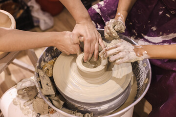 Learning Pottery Workshop. Closeup of teacher woman artist hands, learn student mold clay on pottery wheel. Creative handmade craft. Ceramic art studio.
