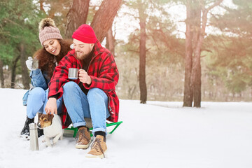 Fototapeta na wymiar Happy young couple with dog in forest on winter day