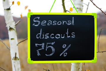 frame with text. seasonal, autumn discounts. Chalkboard and autumn leaves. natural background. the sign with the text weighs on the tree. close-up. 75 percent, sale, big discounts