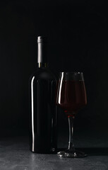 Bottle and glass of red wine on black background