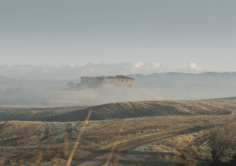 abandoned Tuscan farmhouse in front of rolling hills of Tuscany and covered by morning fog