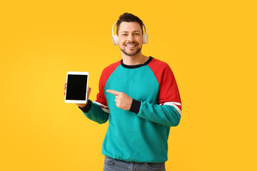 Man with tablet computer and headphones on color background