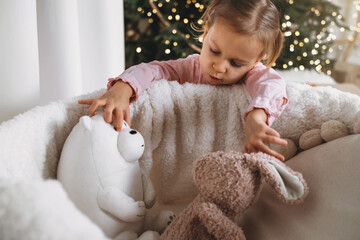 Cute toddler child waiting for presents at home after decorating Christmas tree in eco style with wooden toys. Xmas evening for kids. Nordic style calm preparation. Sad girl