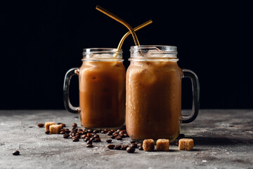 Mason jars of tasty iced coffee with milk, beans and sugar cubes on table