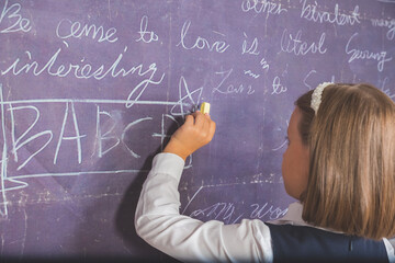 Left Hand writing on a blackboard in white.Cute little girl writing, DRAWING something on chalkboard in a classroom