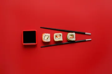 Foto op Canvas Heerlijke sushibroodjes, eetstokjes en kom met sojasaus op kleurenachtergrond © Pixel-Shot