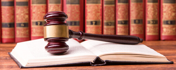 Law concept - Open law book with a wooden judges gavel on table in a courtroom or law enforcement...