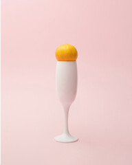 One white champagne glass with one small orange fruit on pink pastel background. Minimal party design.