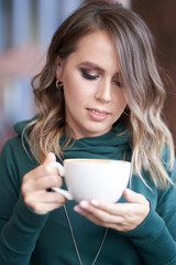 A beautiful woman holding a cup of coffee is sitting in a cafe. She looks directly at the coffee cup with a smile. High quality photo