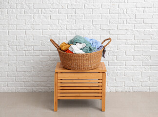 Wicker basket with laundry on chest of drawers near white brick wall
