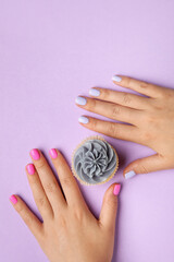 Woman with different color nails and cupcake on purple background, closeup