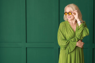 Beautiful mature woman in sunglasses on green background