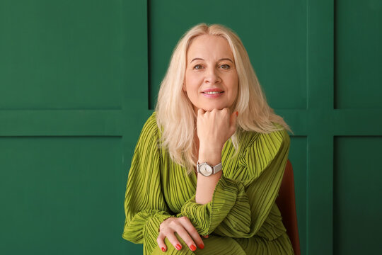 Beautiful Mature Woman Sitting In Chair On Green Background