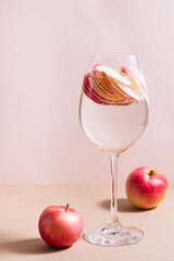 Refreshing cocktail of apple pieces and mineral water in a glass on a pink background. Detox wellbeing drink. Vertical view