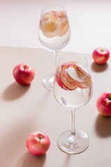 Refreshing cocktail of apple pieces and mineral water in glasses on a brown background in harsh light. Detox wellbeing drink. Vertical view