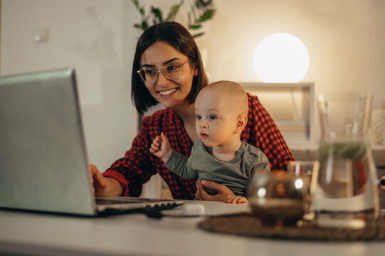 Beautiful business mom using a laptop and spending time with her baby boy at home