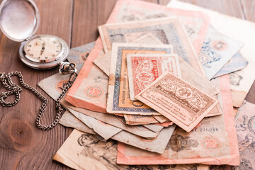 A stack of old outdated ruble bills and a frayed watch on a chain on a wooden table