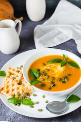 Ready-to-eat pumpkin puree soup with pumpkin seeds, basil leaves and toast in a plate on the table. Vegetarian food. Thanksgiving Day. Vertical view. Close-up