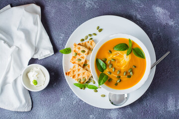 Ready-to-eat pumpkin puree soup with pumpkin seeds, basil leaves and toast in a plate on the table. Vegetarian food. Thanksgiving Day. Top view